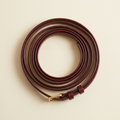 Coraline fine burgundy belt with a slim gold pin buckle, coiled on a cream studio backdrop